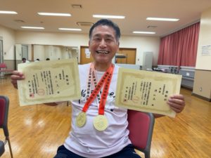 太極拳の世界大会（2種目）の表彰状と金メダルを持って、笑顔の澤さん