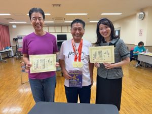 金メダル（2つ）をかけた澤さん 表彰状を持った団長、おにたんと一緒に。