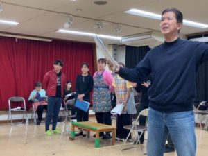 何かを話す団長、後ろで観ている登場人物たち