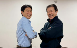 お互い腕を組み、斜めに構えたポーズでにこやかに写真に納まるボイス・エマノンさんと団長