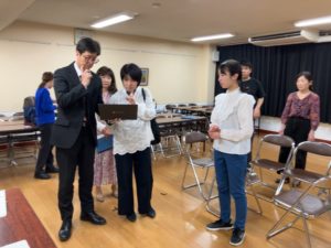 パソコンを手に舞台説明をする団長、取り囲む役者たち